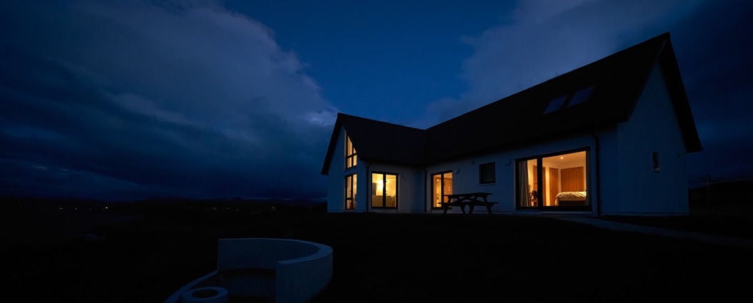 A modern house with glowing interior lights stands against a dark, cloudy night sky, illustrating home power during an outage.