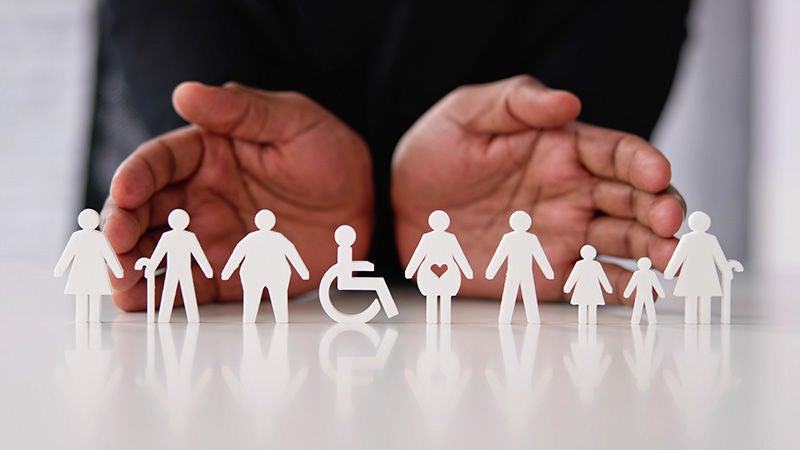 Hands displaying diverse and differently-abled paper figures representing inclusion and belonging