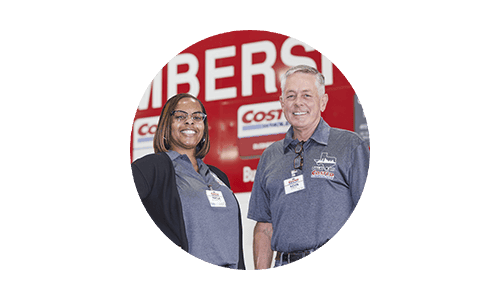 Two Costco employees (female and male) smiling and standing in front of Costco Membership sign