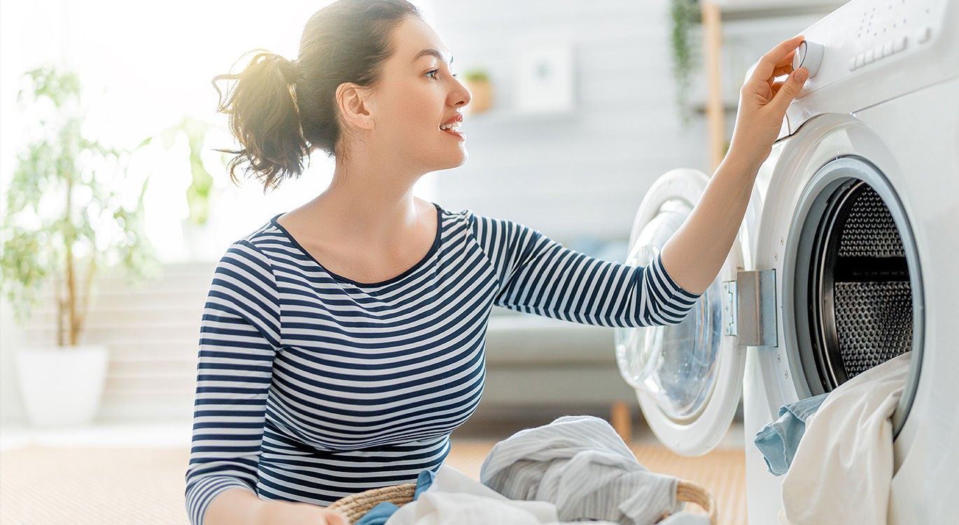 A woman with laundry, kneeling at her washer