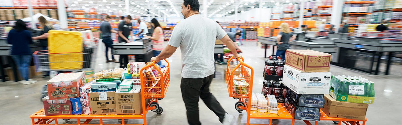 A Costco member pushing two loaded shopping carts inside an official Costco warehouse