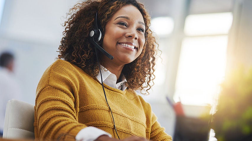 A woman with a headset smiling at her computer