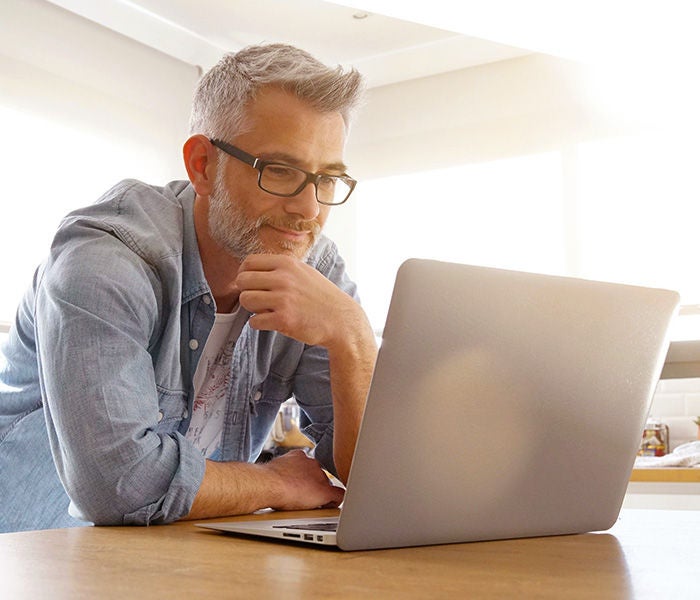 A man looking at his laptop computer while in his kitchen