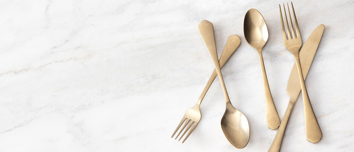 Gold flatware, including forks, spoons, and a knife, arranged on a white marble background.