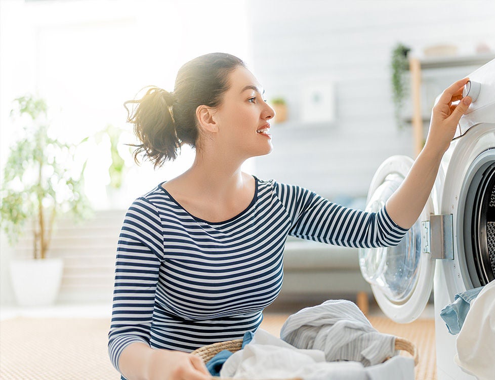 A woman with laundry, kneeling at her washer