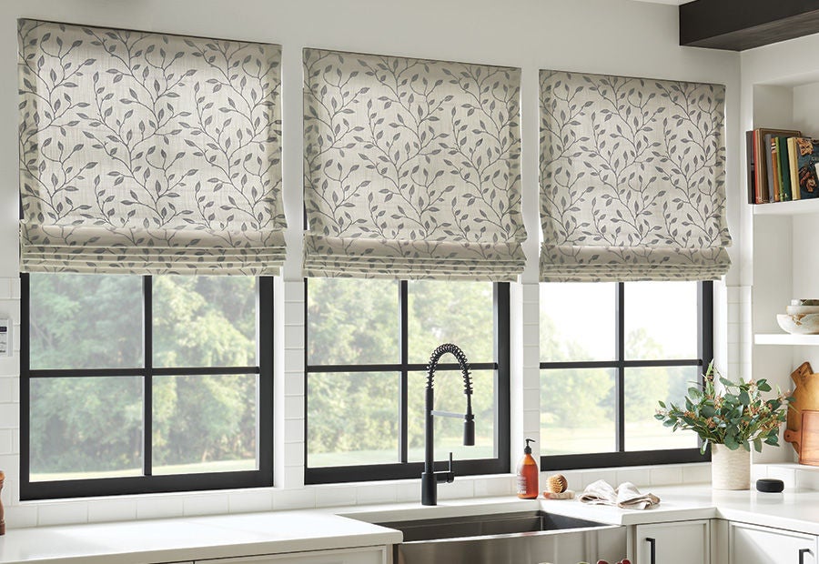 Three gray and white leaf-patterned Bali Roman shades over black-framed kitchen windows.