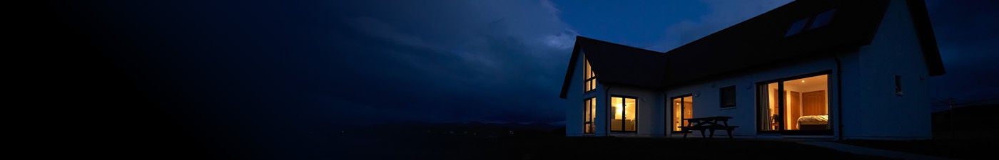 A modern house with glowing interior lights stands against a dark, cloudy night sky, illustrating home power during an outage.