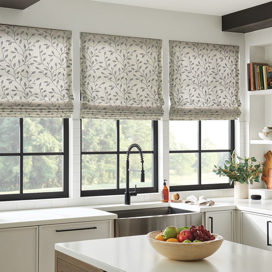 Three gray and white leaf-patterned Bali Roman shades over black-framed kitchen windows.
