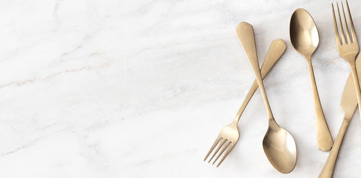 Gold flatware, including forks, spoons, and a knife, arranged on a white marble background.