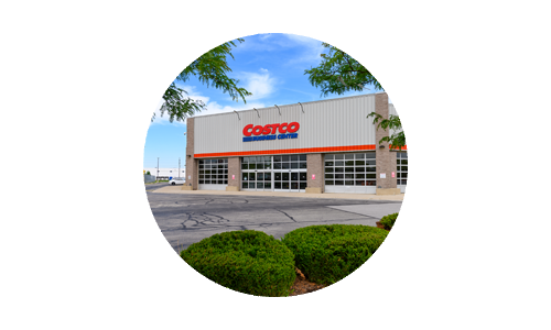 Costco building entrance framed by green trees and shrubs