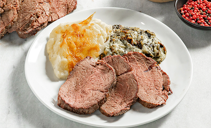 Sliced roast beef served on a plate with scalloped potatoes and creamed spinach